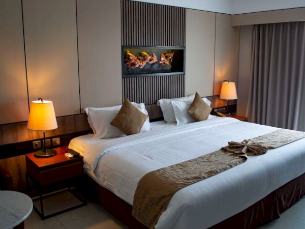 A hotel room with a large bed, decorative pillows, bedside lamps, and a wall-mounted display, all in soft lighting.