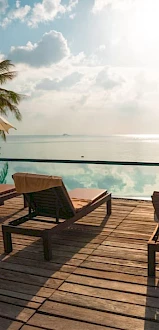 A serene poolside setting features lounge chairs, umbrellas, and a stunning view of the ocean under a partly cloudy sky.