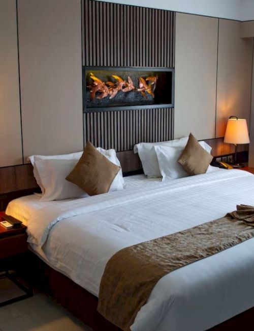 A hotel room with a large bed, bedside tables, lamps, and modern decor. Beige tones and soft lighting create a cozy atmosphere.