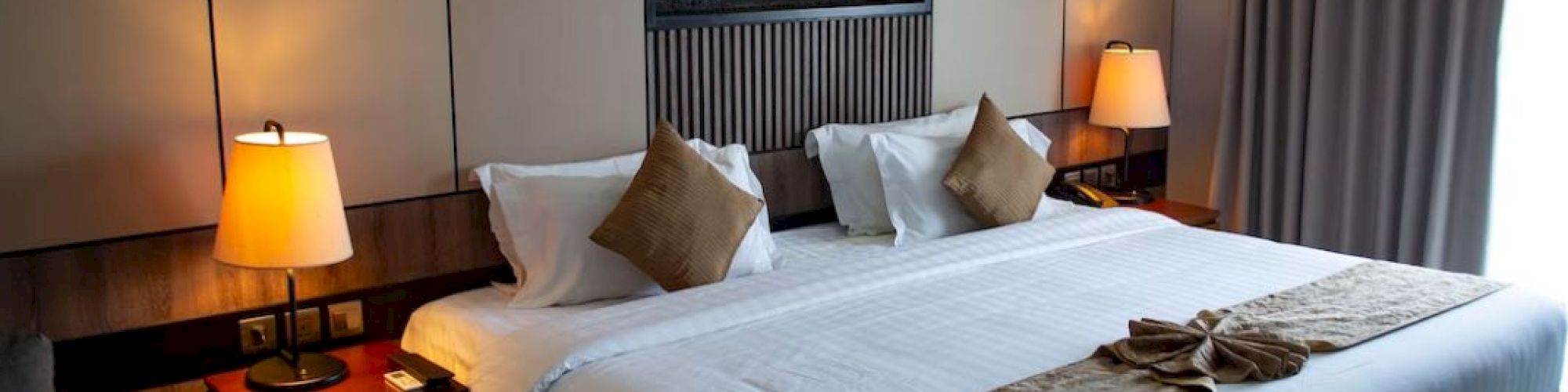 A cozy hotel room with a large bed, warm lighting, and elegant decor, featuring lamps and a modern artwork on the wall.