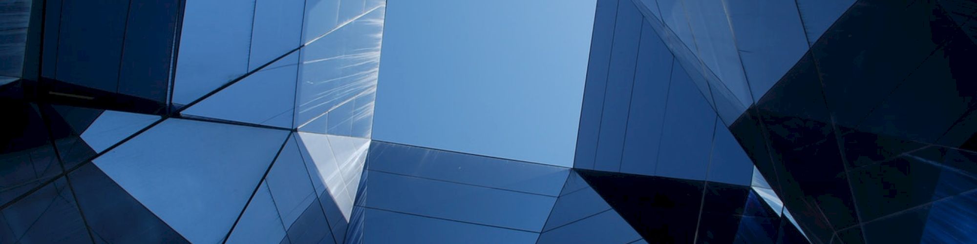 Geometric architecture with reflective glass panels and a central opening to the sky, capturing a modern, abstract design perspective.