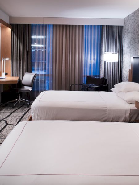 The image shows a modern hotel room with two beds, a desk, a TV, and stylish decor ending the sentence.