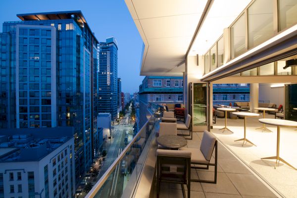 Modern city view with tall buildings, an outdoor terrace with seating, and a well-lit indoor area.