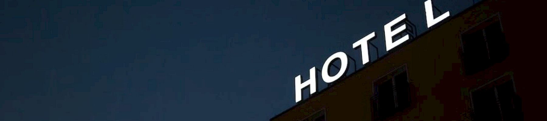 A building at night with a large illuminated sign saying "HOTEL" on its rooftop.