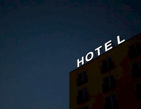 A building at night with a large illuminated sign saying "HOTEL" on its rooftop.