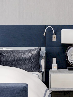A stylish bedroom with a navy blue headboard, decorative pillows, and a nightstand with a lamp and decorative piece.