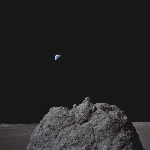 A rocky lunar landscape with Earth rising in the distant dark sky.