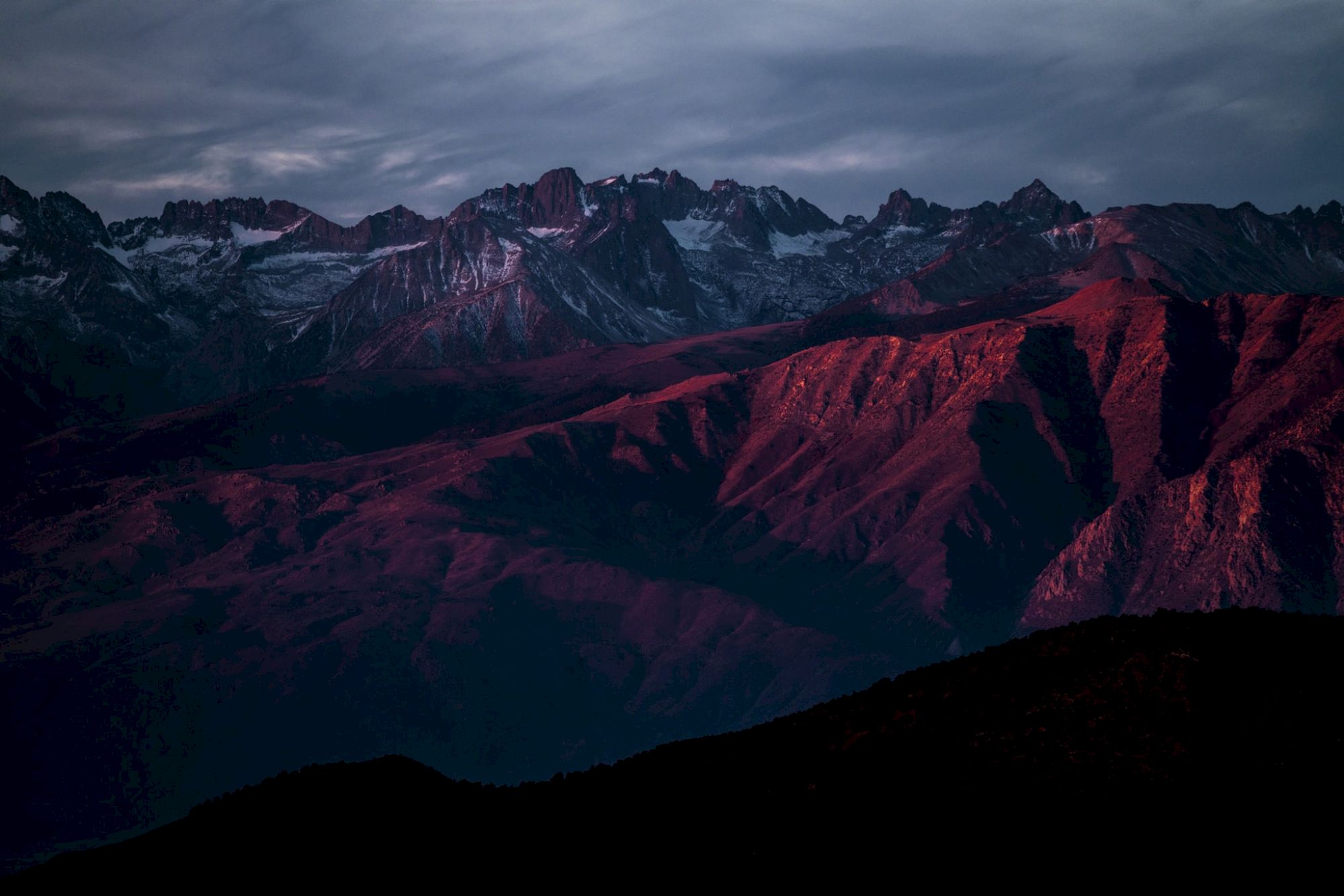A mountain range illuminated by red sunlight under a dramatic sky.