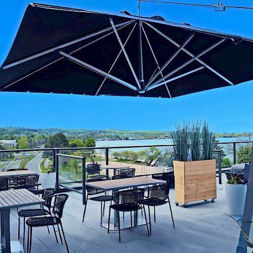 A rooftop patio with tables, chairs, a large umbrella, and scenic views, featuring modern outdoor furniture and clear blue skies.