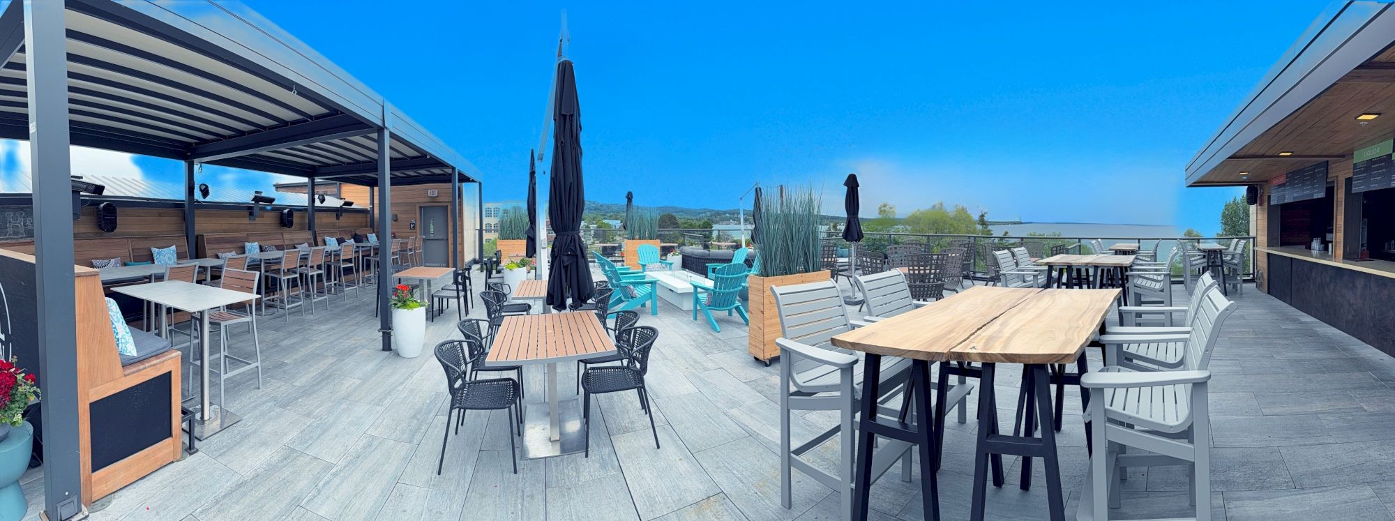 Spacious outdoor patio with diverse seating, tables, and a canopy, overlooking a scenic view under a clear blue sky.