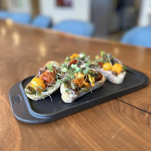 Slices of bread topped with roasted vegetables and greens on a dark serving tray, placed on a wooden table.