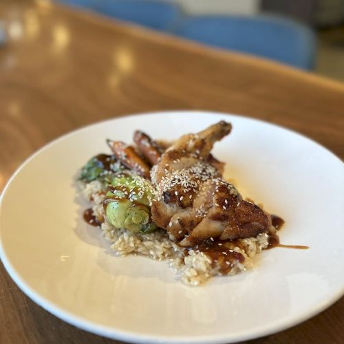A dish featuring chicken, rice, and vegetables, topped with sesame seeds, served on a round white plate.