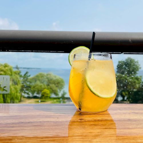 A refreshing cocktail with lime garnish on a wooden table, overlooking a scenic view of trees and water in the background.