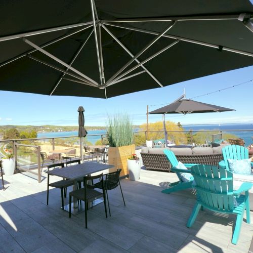 A spacious outdoor deck features tables, chairs, and large umbrellas, overlooking a scenic view of water and landscape in the distance.
