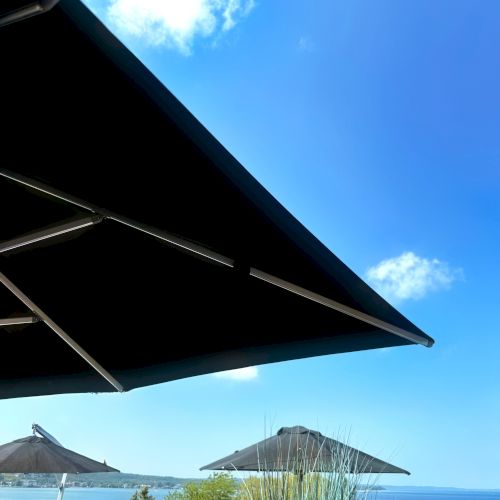 A scenic view of a patio with umbrellas, chairs, and a vibrant blue sky overlooking the ocean in the background.