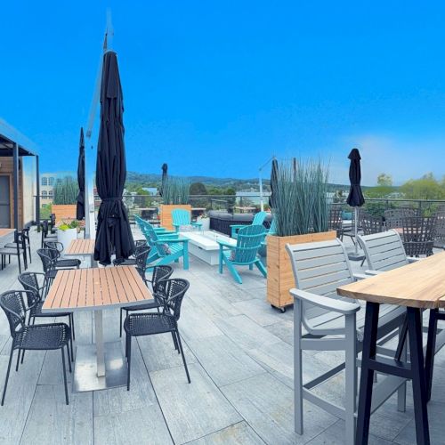 Rooftop bar with various seating, tables, umbrellas, and a view of the landscape under a clear blue sky.