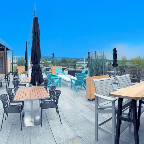 It's a rooftop patio with tables, chairs, and umbrellas under a clear blue sky, set for dining and relaxation with a scenic view.