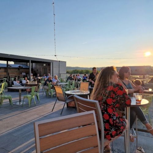 People are relaxing on a rooftop terrace during sunset, enjoying drinks and conversation.