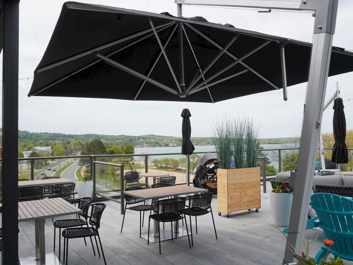A rooftop patio with chairs, tables, and a large umbrella overlooks a scenic landscape with trees and distant hills.
