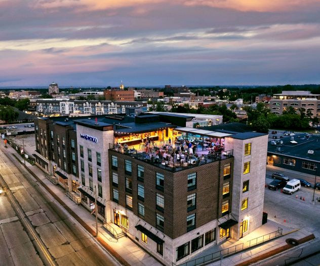 Aerial view of a city at sunset, featuring a multi-story building with a busy rooftop area and surrounding streets.