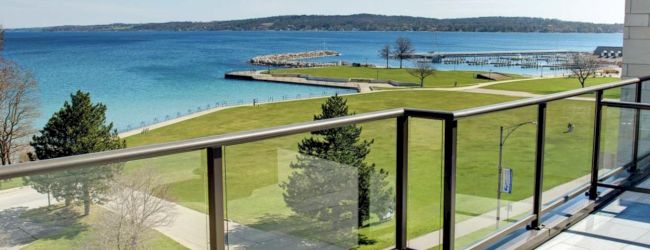 A scenic view from a balcony overlooking a grassy area and a body of water, with a clear blue sky above.