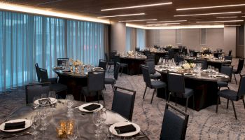A dining room with round tables set for a formal event, featuring elegant tableware, chairs, and dim lighting.