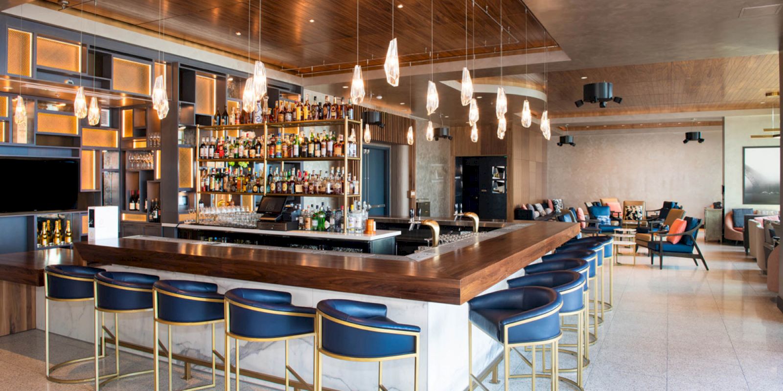 A stylish bar with hanging lights, blue barstools, and a stocked back bar is depicted in the modern space.