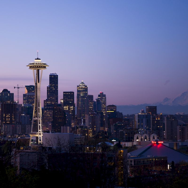 Seattle skyline with the Space Needle at dusk, and Mount Rainier visible in the distance.