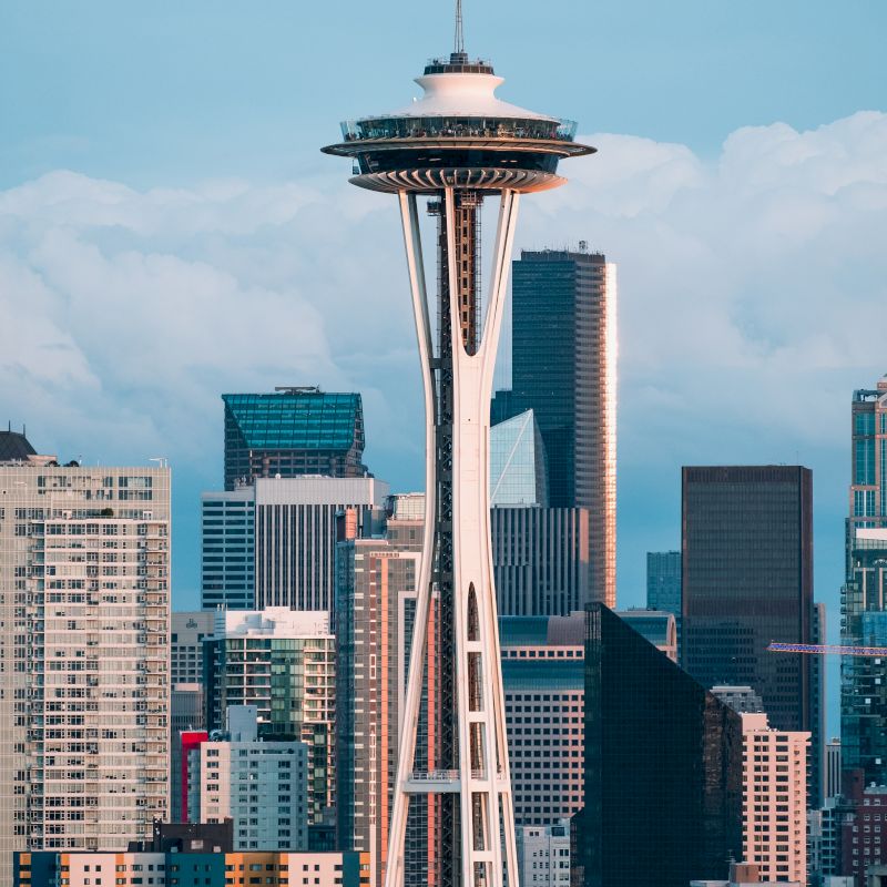 The image shows the Seattle skyline featuring the Space Needle with surrounding skyscrapers against a backdrop of cloudy skies.