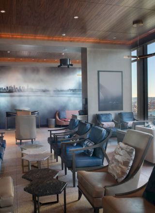 A modern lounge with comfortable seating, a wall mural, and large windows offering a scenic view of the skyline and water outside.