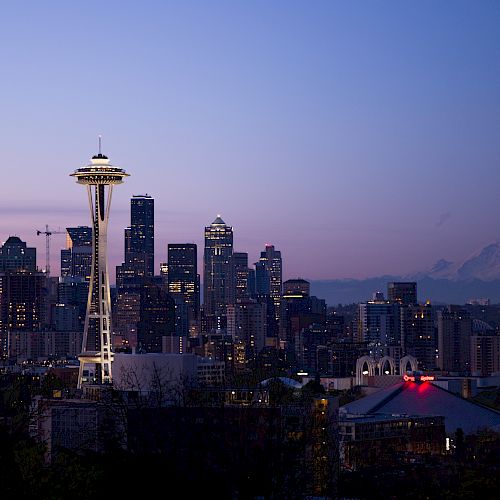 Seattle skyline at dusk featuring the Space Needle, illuminated city buildings, and Mount Rainier in the background.