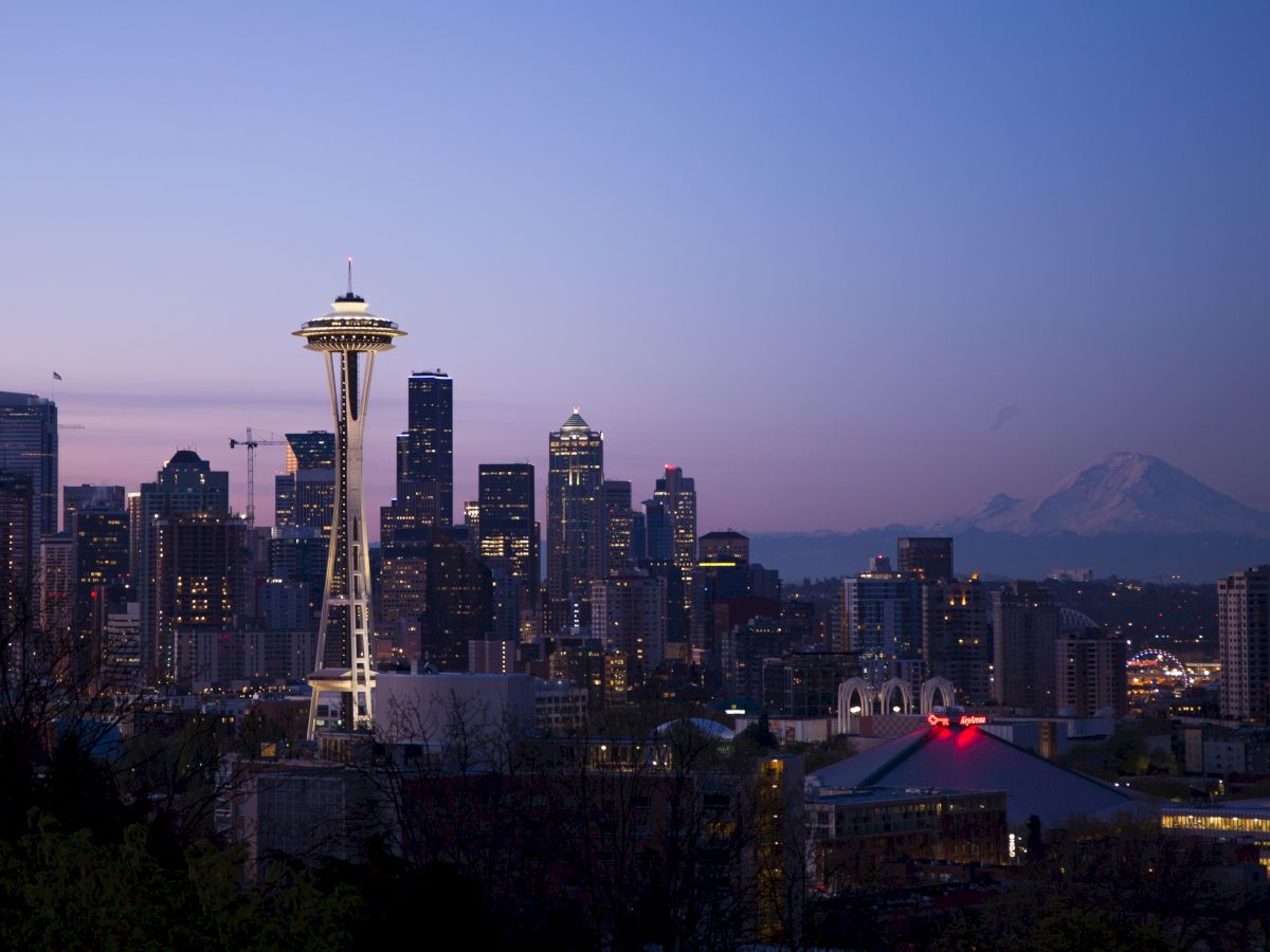 Seattle skyline at dusk with the Space Needle visible and Mount Rainier in the background, creating a picturesque urban scene.