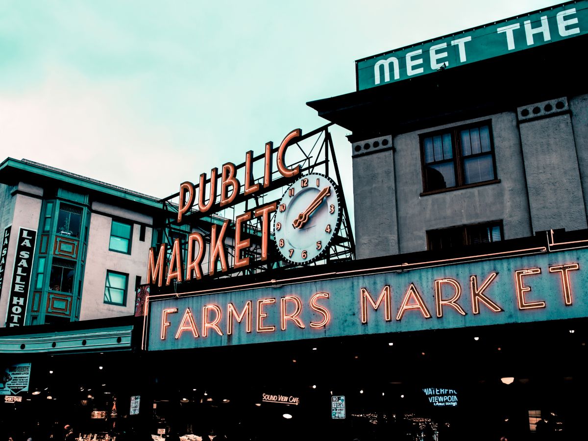 Neon signs for "PUBLIC MARKET" and "FARMERS MARKET" in front of a building with "MEET THE" partially visible on top.