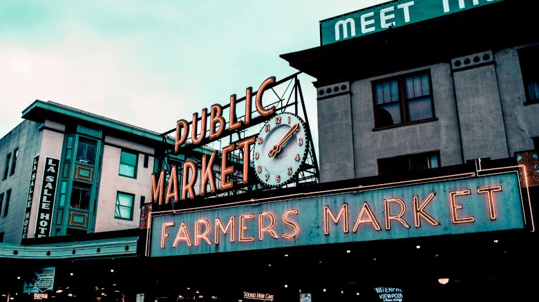 Neon signs for "PUBLIC MARKET" and "FARMERS MARKET" in front of a building with "MEET THE" partially visible on top.