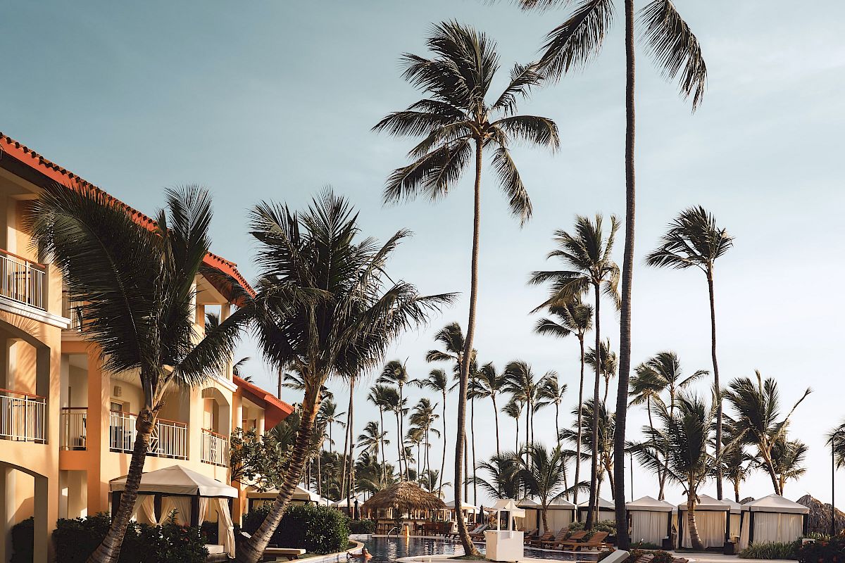 A serene poolside scene with lounge chairs, tall palm trees, and a multi-story building under a clear sky.